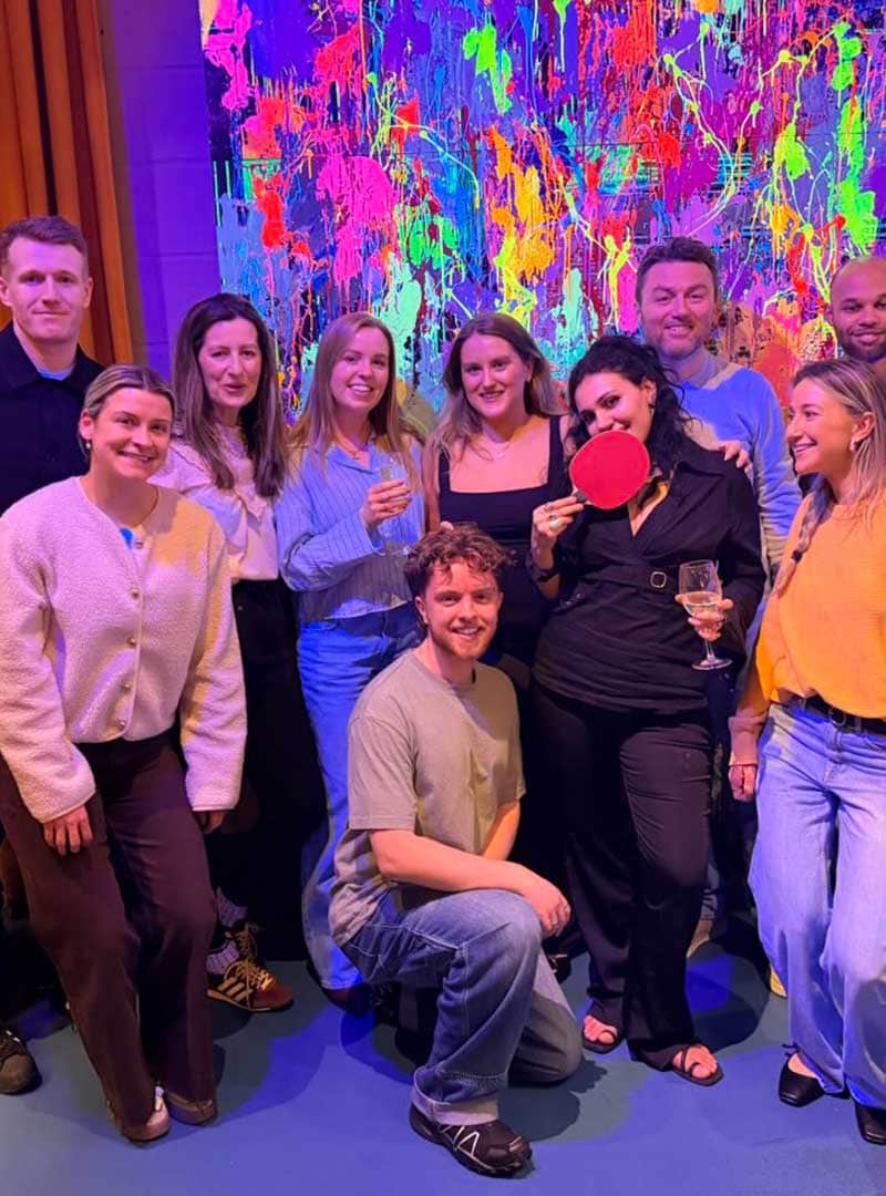 Group of professionals celebrating at a corporate event with vibrant artwork in the background.